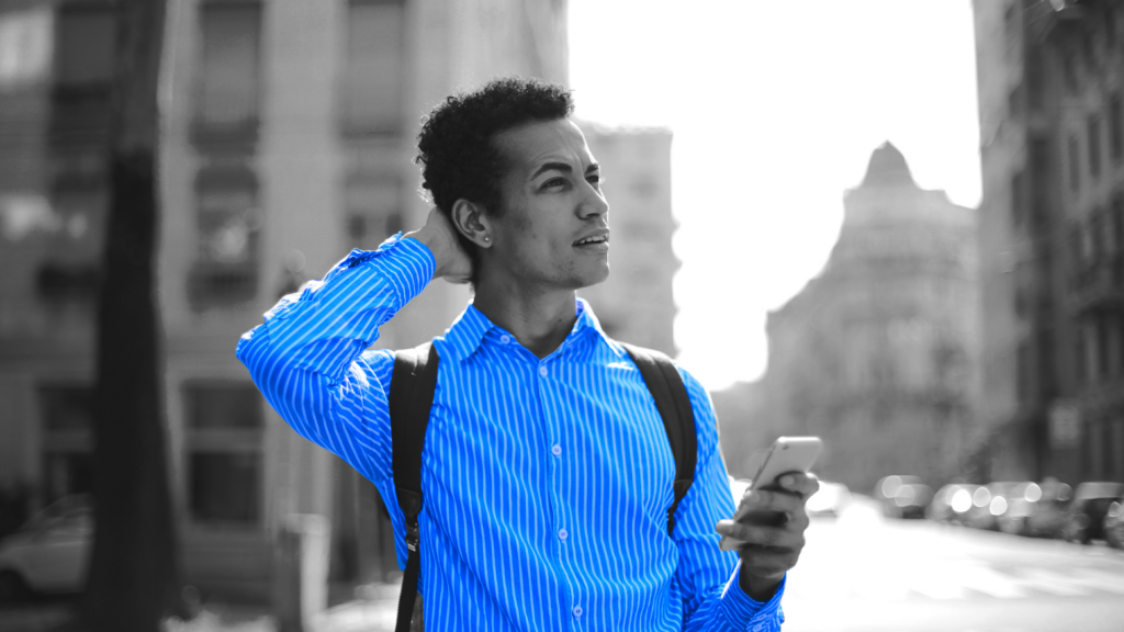 Mężczyzna w niebieskiej koszuli z plecakiem trzyma w ręce telefon i patrzy do góry.