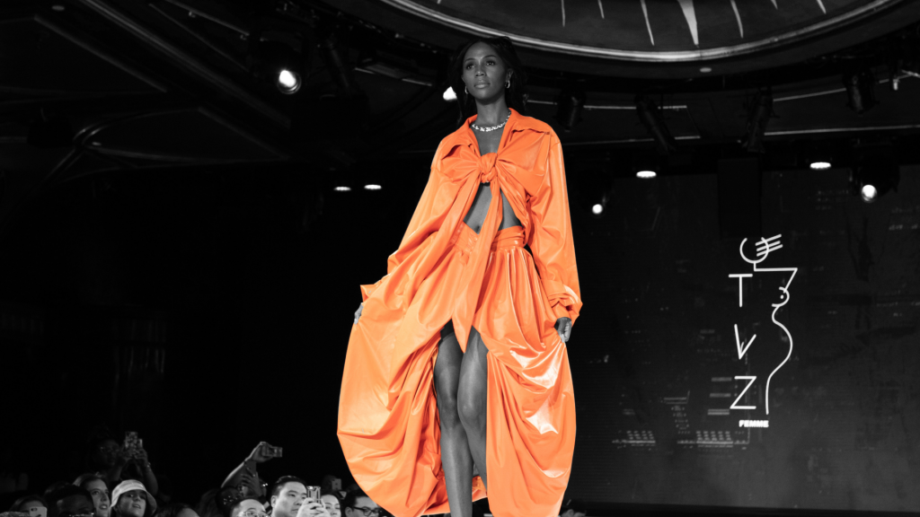 Modelka idąca po wybiegu w pomarańczowym stroju podczas pokazu mody.