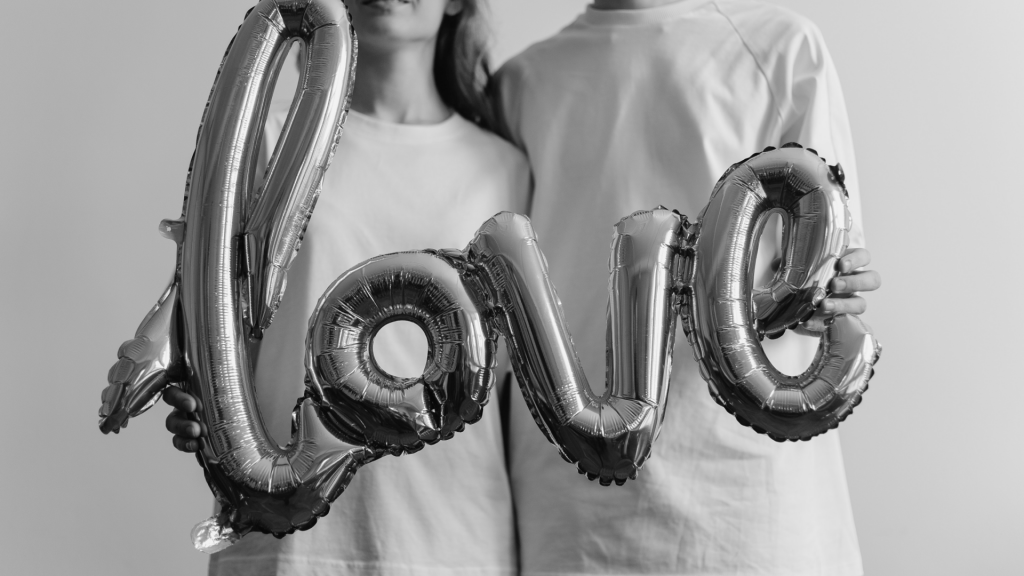 Czarno białe zdjęcie pary trzymającej balon w kształcie napisu "love".