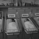 Czarno-białe zdjęcie oddziału noworodkowego we włoskim szpitalu. W szeregu ustawione są łóżeczka z niemowlętami, a przy każdym z nich widoczna jest karteczka z nietypowym imieniem, np. „Crocifissa”, „Pasquale” czy „Fortunato”.