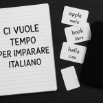 Czarno-białe zdjęcie przedstawia materiały do nauki języka włoskiego: mały notes z napisem „ci vuole tempo per imparare italiano”, telefon komórkowy oraz fiszki leżące obok na stole.
