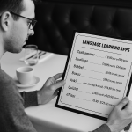 A black-and-white photograph of a person sitting at a restaurant table, examining a menu where instead of food items, language learning apps and their real prices are listed. The scene conveys a creative comparison between choosing meals and selecting affordable language apps.