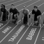 The black-and-white photo shows six runners - men and women - lined up at the starting line of a six-lane treadmill. Each track bears the name of the application: DUOLINGO, BUSUU, ANKI, TAALHAMMER, BABBEL and LINGQ. The figures are focused and ready to start, and the slightly overhead perspective emphasizes the symmetry and tension of the moment before the run.