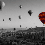 Black-and-white panoramic view of Cappadocia with multiple hot air balloons in the sky, one balloon in vibrant color standing out against the monochrome landscape, symbolizing focus and distinction in a language learning journey.