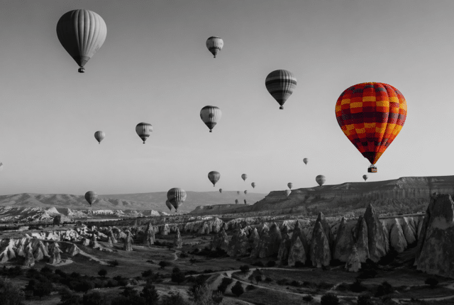 Black-and-white panoramic view of Cappadocia with multiple hot air balloons in the sky, one balloon in vibrant color standing out against the monochrome landscape, symbolizing focus and distinction in a language learning journey.