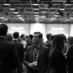 Black-and-white image of a professional at a networking event, listening to conversations around them while hesitating to join in, illustrating the gap between knowing vocabulary and speaking fluently.