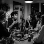 Ultrarealistic black-and-white 16:9 image of a group of friends having an animated late-night conversation around a crowded kitchen table, capturing language as one integrated system through spontaneous speaking, listening, emotional reactions, and real-time social interaction.